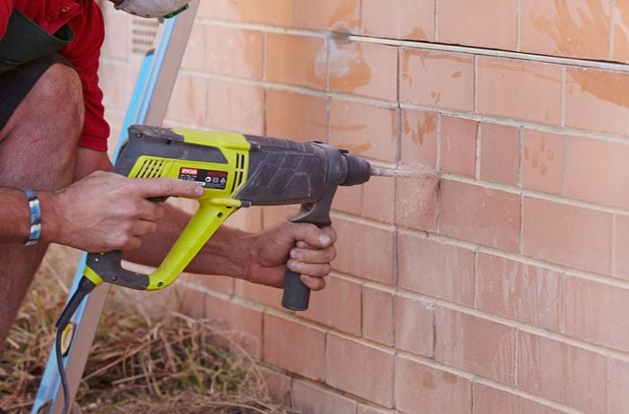 A hammer drill being used to loosen mortar between bricks