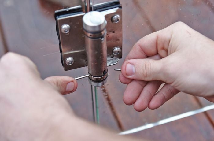 Person using a pin to add tension to gate hinge.