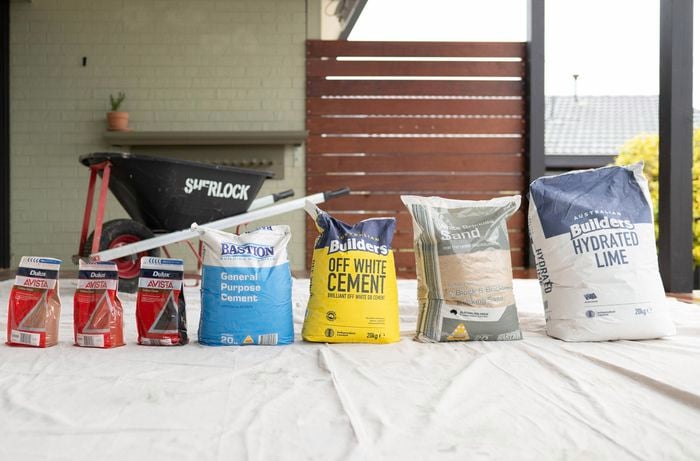 A variety of mortar mix, including cement, sand, lime, oxide color powders, and a bonding agent, are neatly arranged on a covered floor. 