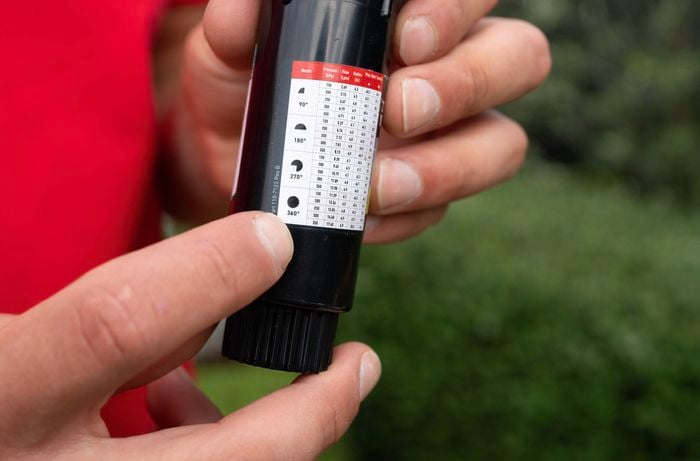 A person is holding a pop-up sprinkler head, pointing to a spray distance chart.