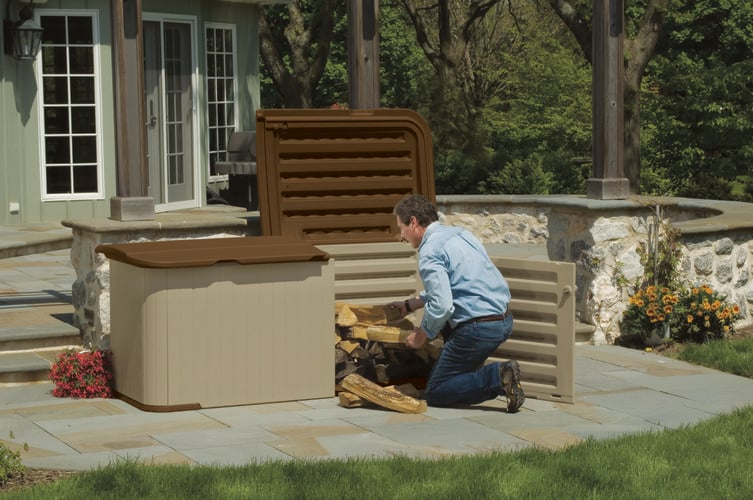 Man kneeling in an outdoor paved area placing firewood into storage cabinet with lid and doors