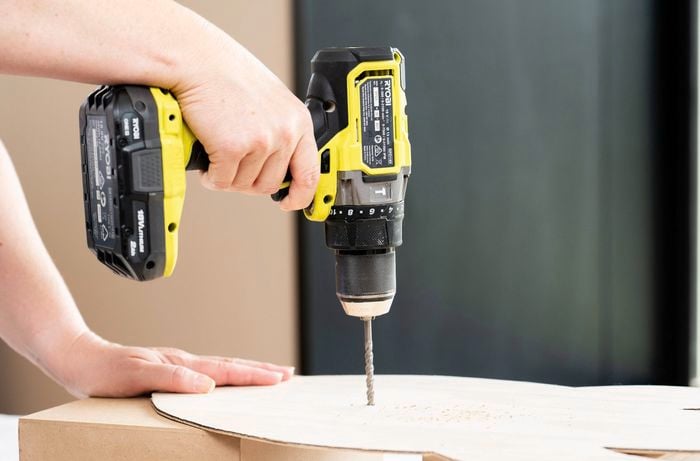 A person is ​drilling​ a centre hole into a plywood rocket shape using a cordless drill for a DIY clock upcycle project.