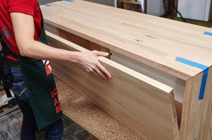 A person fitting a back panel into the sides and top of a timber vanity unit