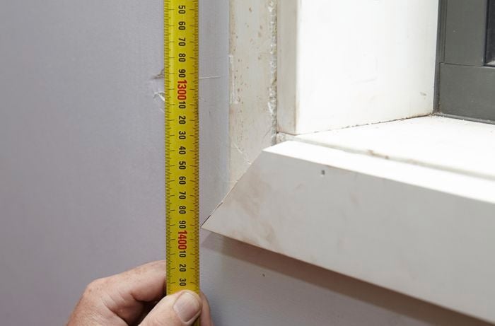 A person measuring the distance to the outside corner of architrave under a window