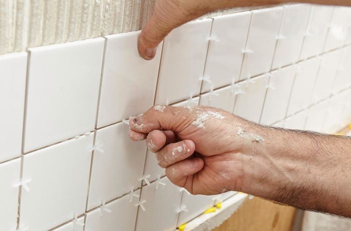 Person putting spacers between tiles that have been freshly laid on the wall.