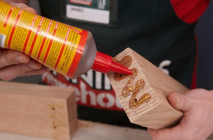 A person applying adhesive to the end of a piece of timber
