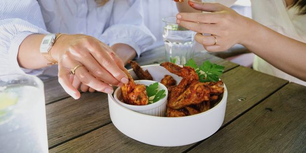 Two people sharing spicy chicken wings with dipping sauce at an outdoor table.