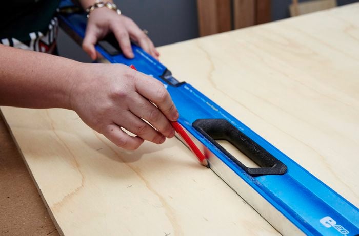 A person drawing a line on a plywood sheet using a spirit level