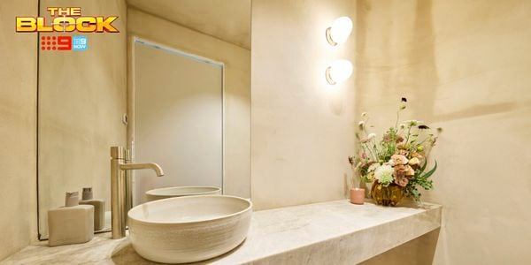 A modern bathroom with a sink on a benchtop with a vase with flowers in it on the benchtop, a mirror and lights on the wall.