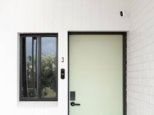 Front door with smart lock, video doorbell and security camera on a white house exterior.