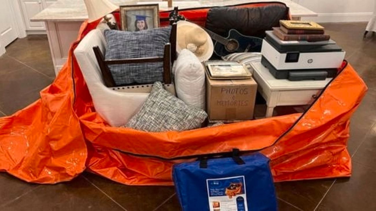 Orange Krisis flood bag with different household items in it on timber flooring inside a house.