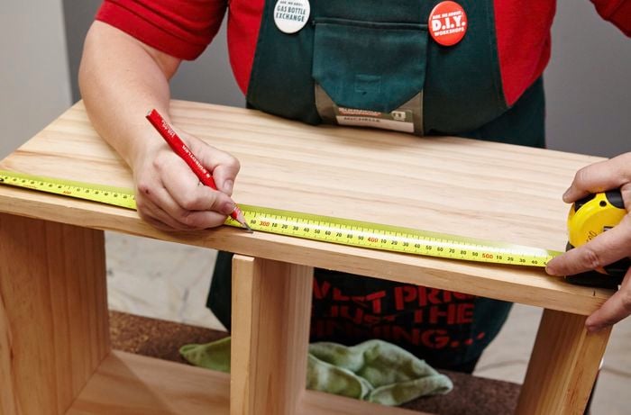 A tape measure and pencil being used to mark a kids wooden storage bench for screw holes