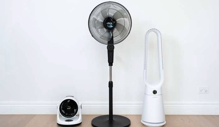 3 Different types of fans sitting a room in front of a wall.