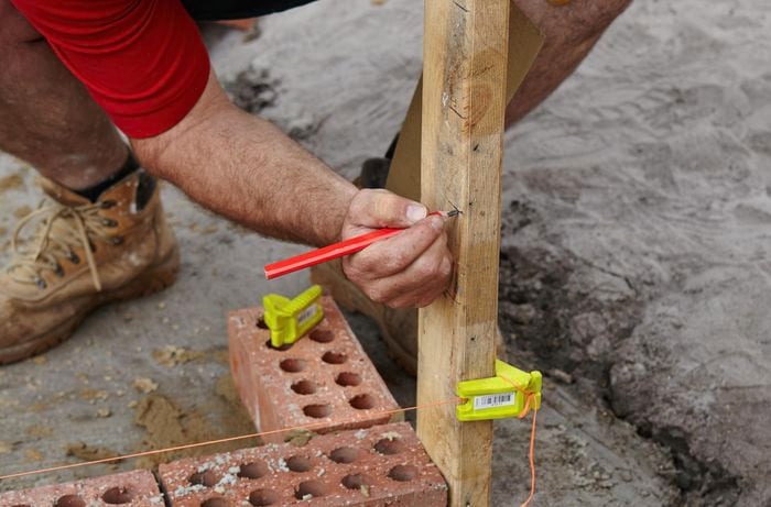 Person marking up a timber plinth that's sitting next to a row of bricks.