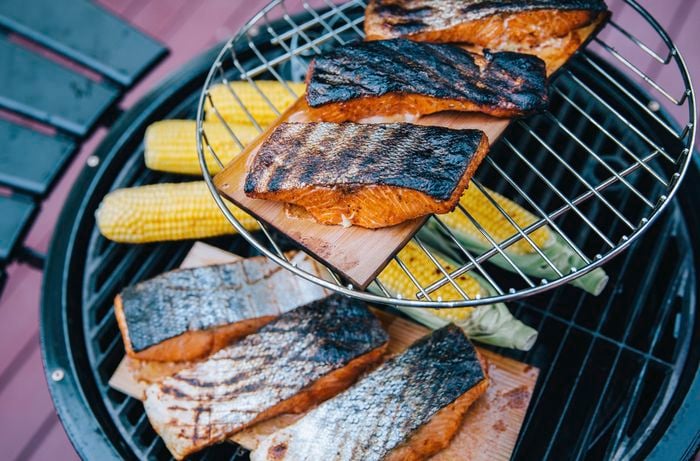Fillets of salmon with charred skin on a serving board with corn cobs on a BBQ