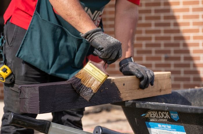 Man applying paint to stump with paint brush.