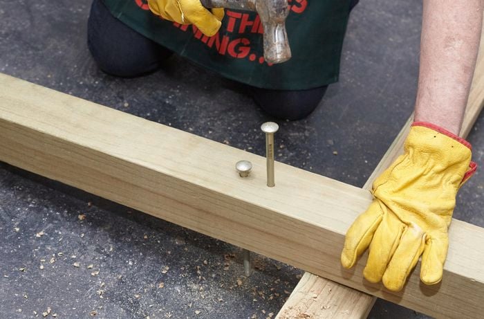Person hammering very long screw into piece of timber.