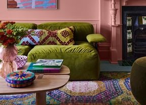 Lounge room with pink walls, a green couch, multi coloured rug and a wooden coffee table in it.