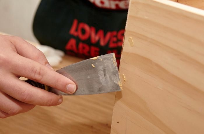 Person filling holes with timber filler and scraper.