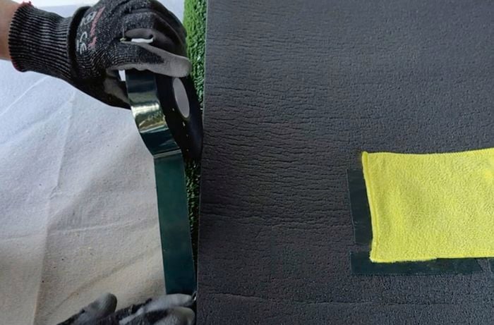 A roll of black tape alongside the back of a foam turf mat with a yellow square