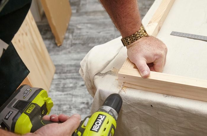 A person drilling holes in the corner of a pine timber frame