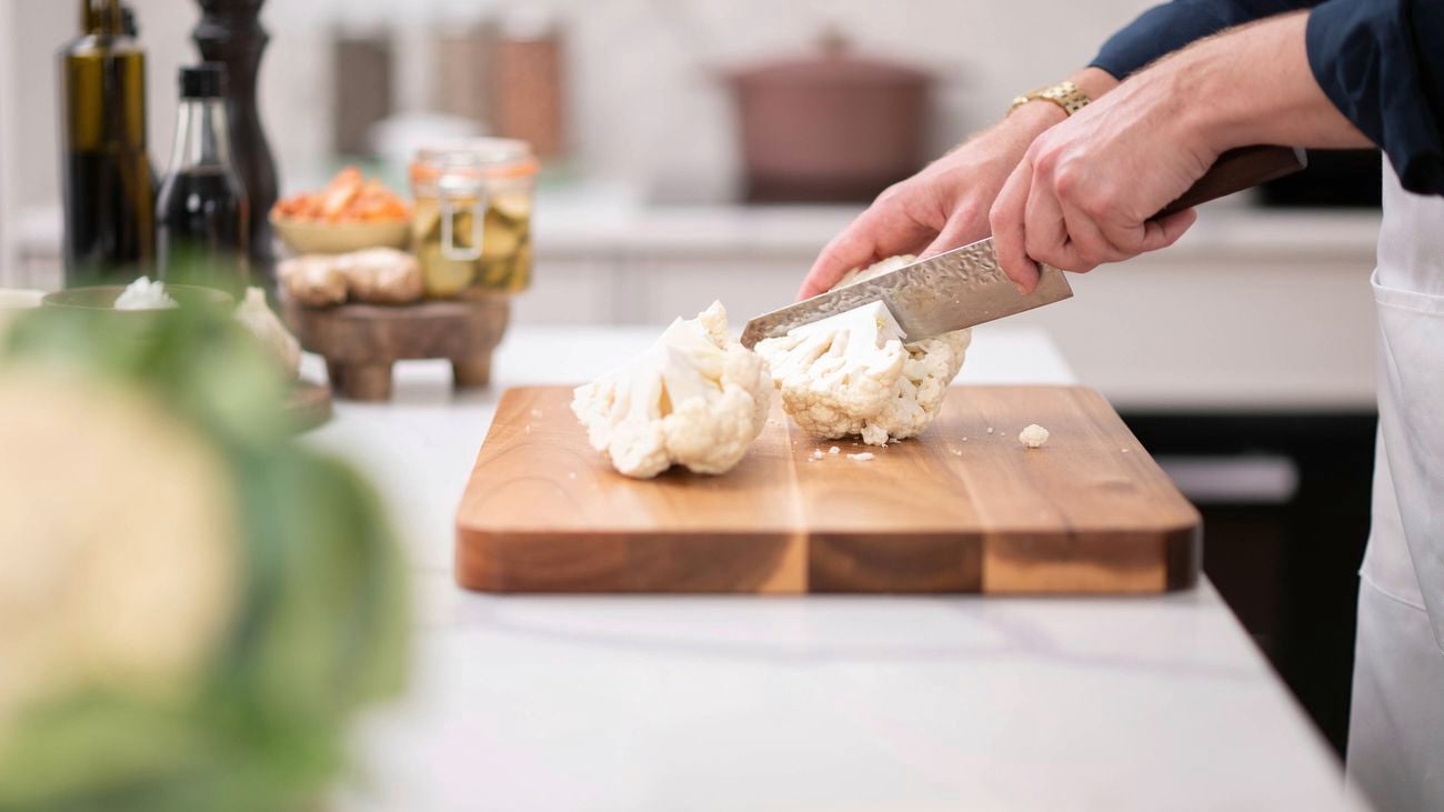 A person is chopping cauliflower with a knife on chopping board