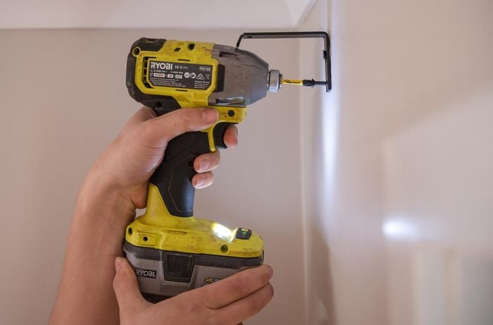 Using a drill to place curtain brackets on a wall