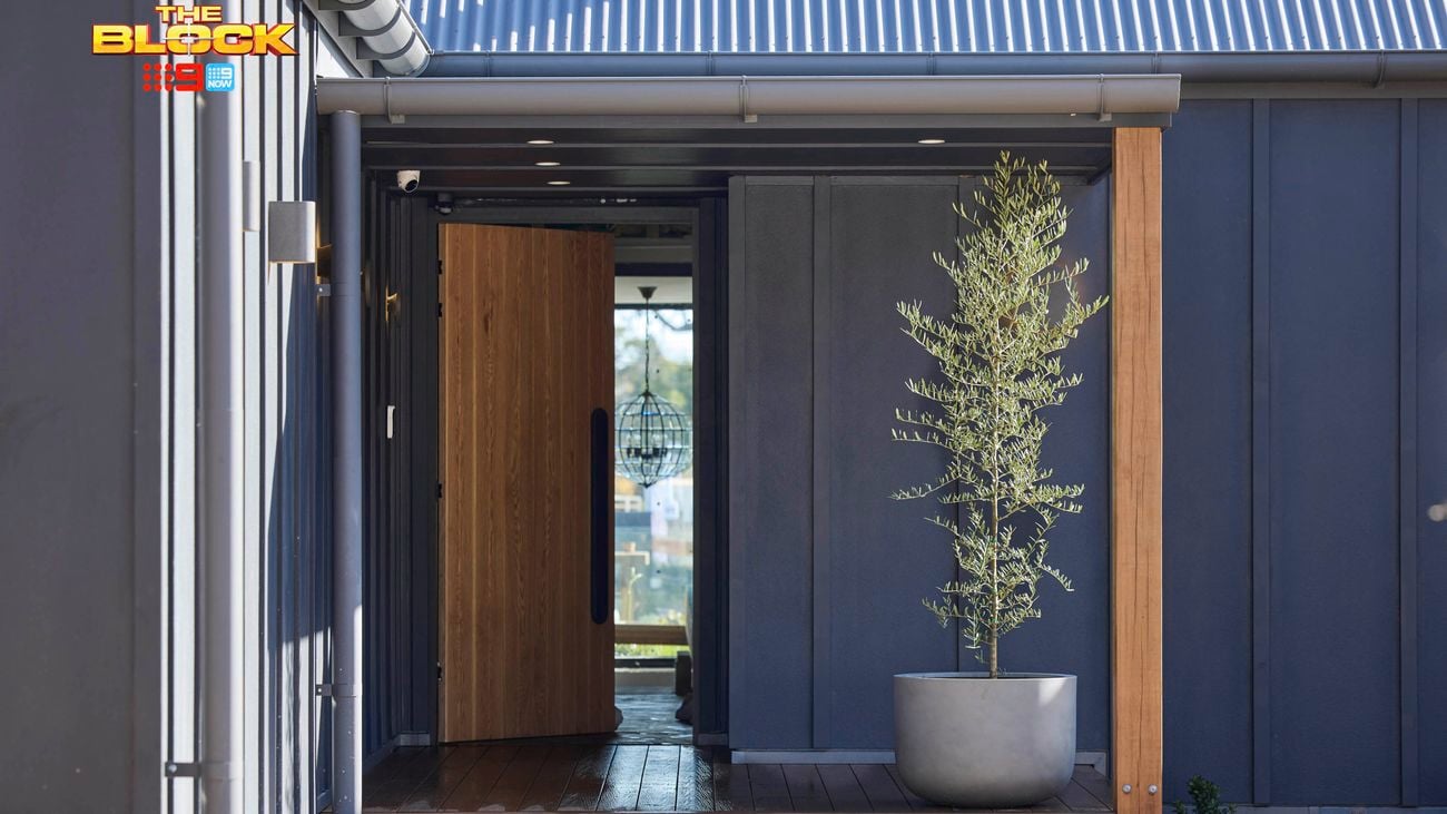 A front entrance of a house with the timber door open and a pot with a tree in it on timber decking.