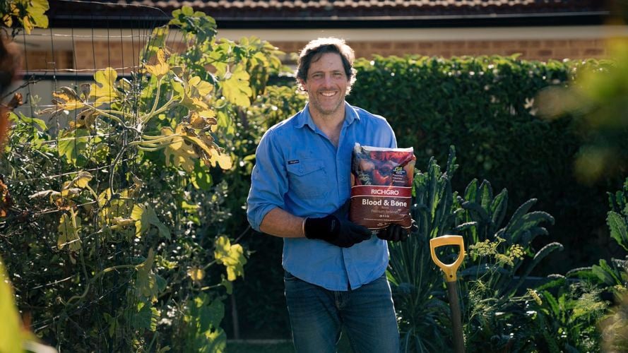 Man standing in garden with fertilizer bag.