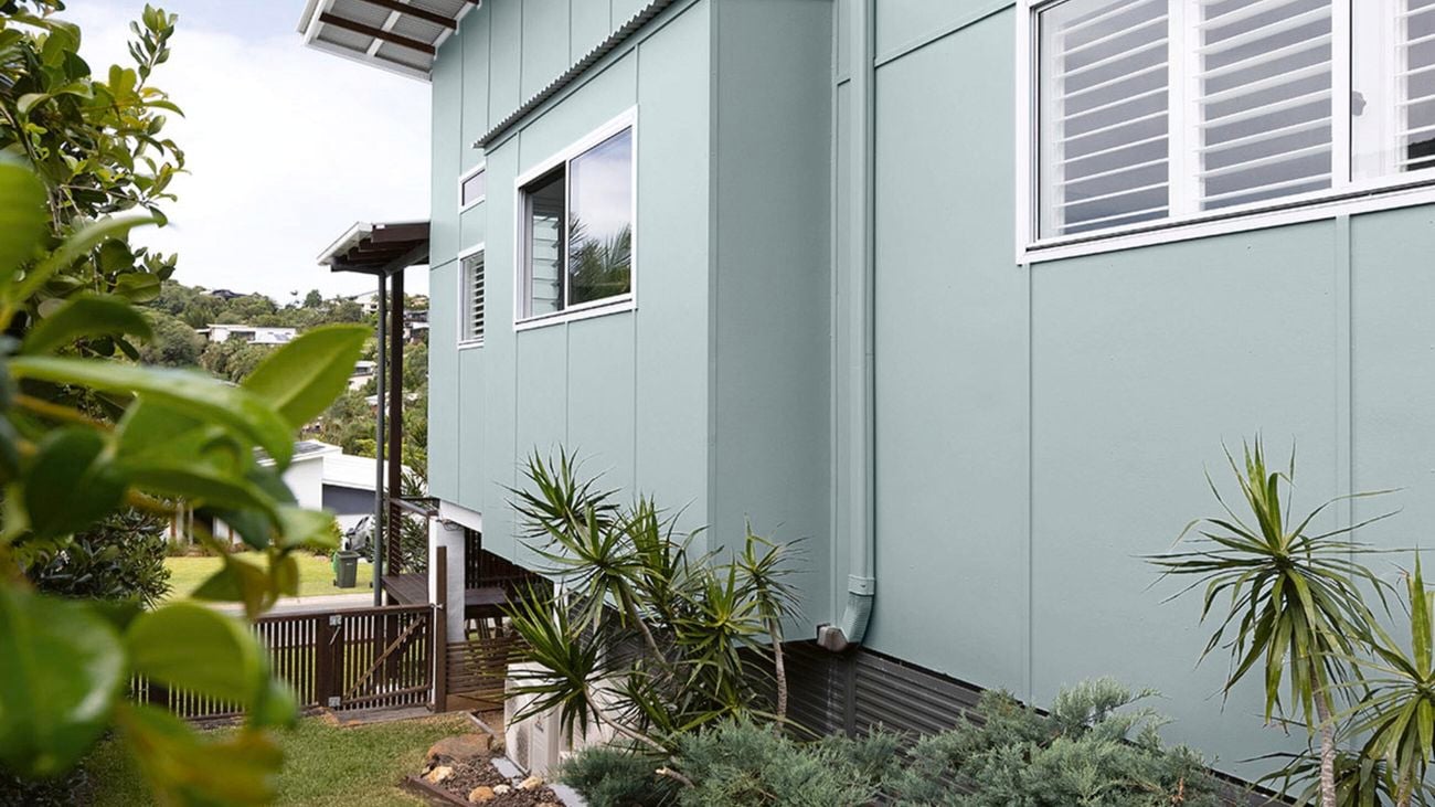 Timber garden beds line the side of a two-storey home painted in Dulux Milky Spearmint