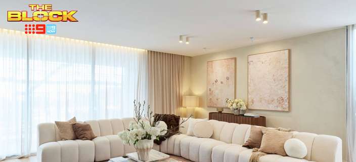 Contemporary living room featuring large curved cream sofas, a stone coffee table, soft pink rug and neutral décor.
