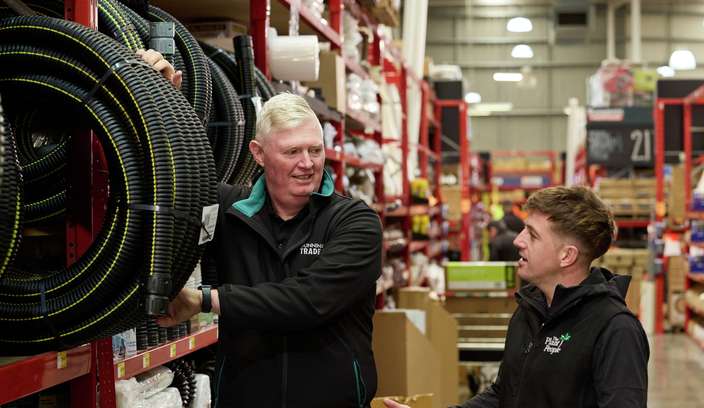 A Bunnings Team Member and a male talking beside a display of flexible hoses in a Bunnings store aisle.