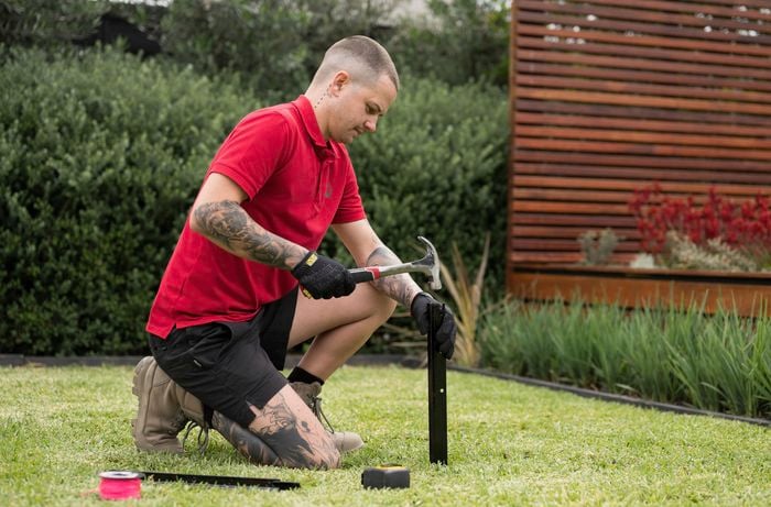 A Bunnings Team Member is placing the stakes in each corner using a hammer to mark a garden bed's perimeter.