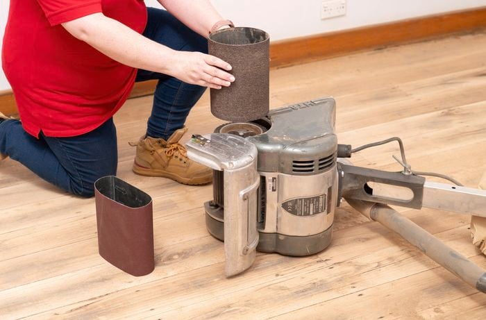 A Bunnings Team Member is fitting a sanding belt onto a drum floor sander to ensure it runs straight and safely before use.