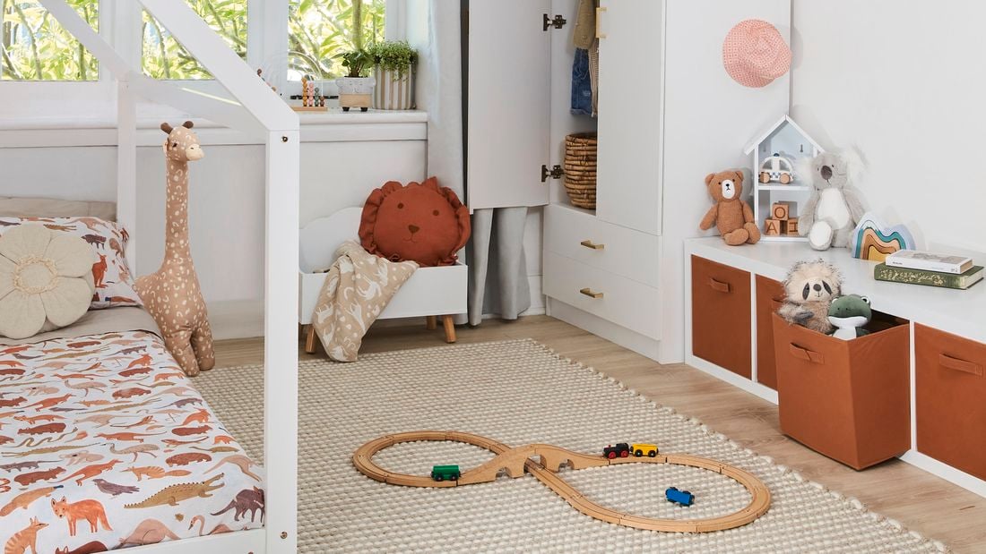 Kids bedroom with white toddler bed and cupboard, printed ceiling light shade and horizontal storage cabinet with brown drawers and white walls