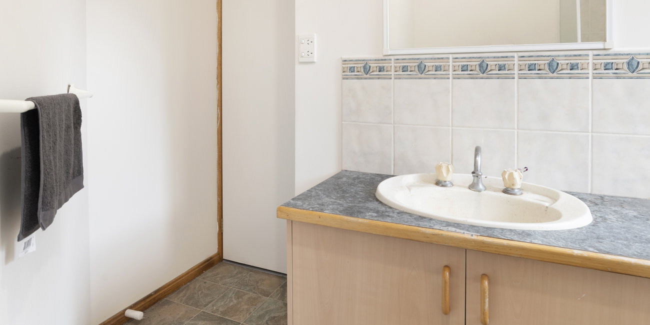 Outdated bathroom with timber cabinets, grey benchtops and cream tiles.