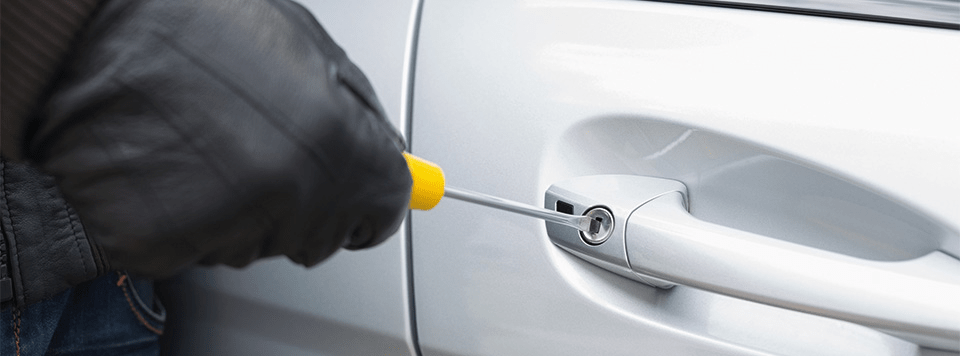 A person trying to break into a car with a screwdriver