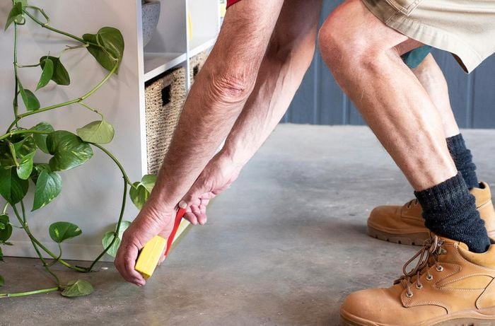 man bent over measuring floor space beside a shelf