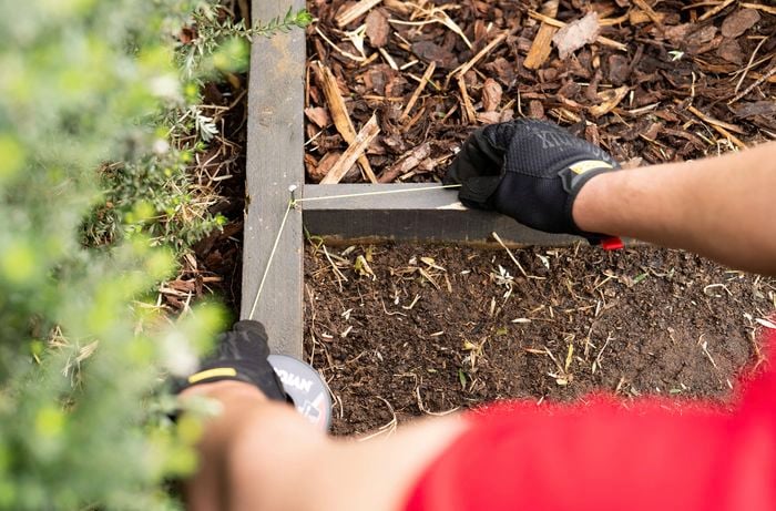 A person wearing gloves is installing timber garden edging, using a string line to keep the edges straight