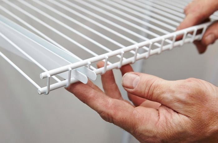 A shelf being fitted to brackets by securing it to the supports and track.