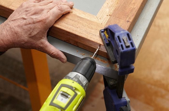 Person drilling into thin bit of timber frame.