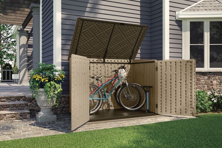 Outdoor paved area beside a house with storage cabinet containing two bikes
