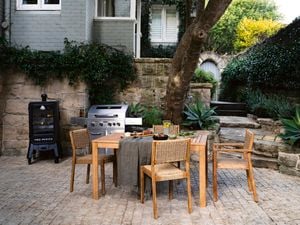 An outdoor dining set in front of a barbecue in a brick paved outdoor courtyard