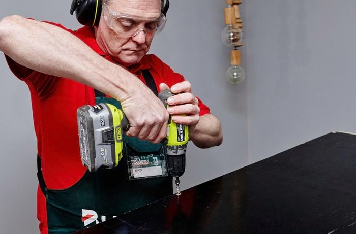 Person drilling nail into cabinet to attach back of cabinet to cabinet