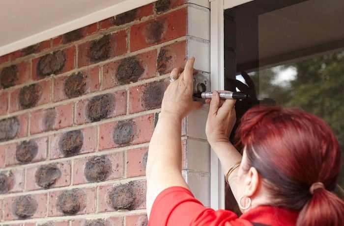 A person marking hole positions for a metal flange on a brick wall