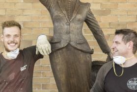 Two people standing with metal sculpture between them