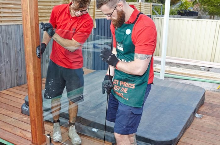 Two people putting glass pool fencing panel in place.