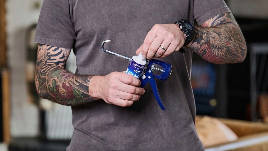 Person holding kitchen and bathroom sealant, and a caulking gun.