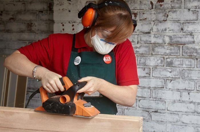 Person wearing face mask, eye protection and earmuffs sanding a piece of timber.