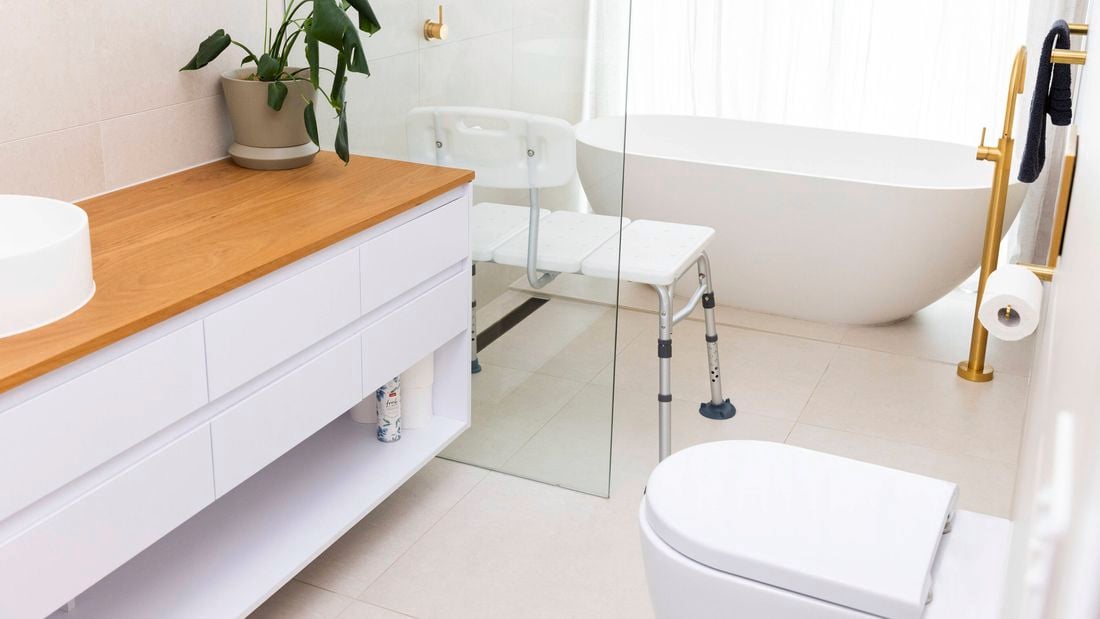 Bathroom with white bathroon cabinet with timber top, toilet, free standing bath and assited bench